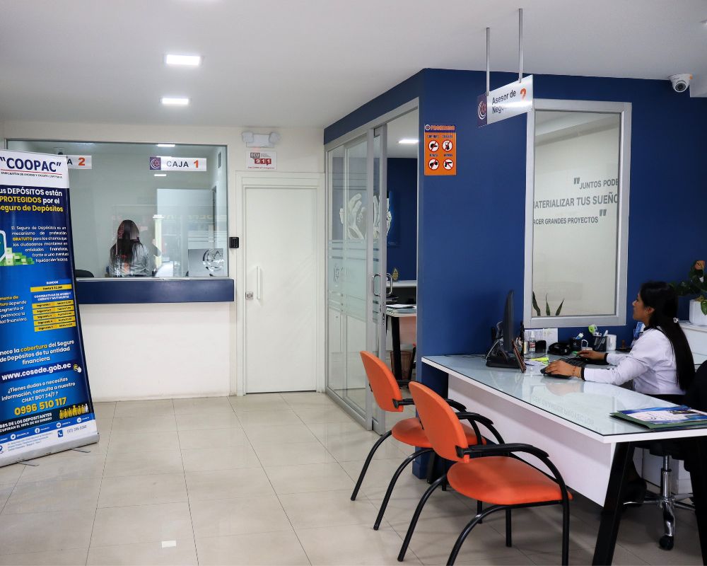 Interior de la agencia Loja de COOPAC, con ventanilla de caja y atención de una asesora